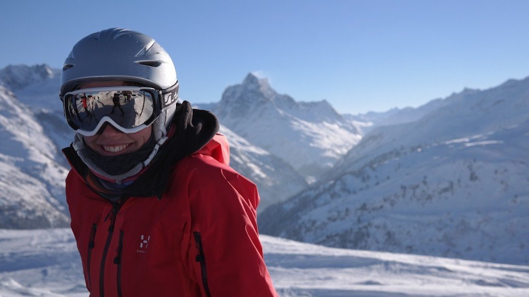 A person in a red coat wears anti-fog ski goggles on a sunny day in the snow.