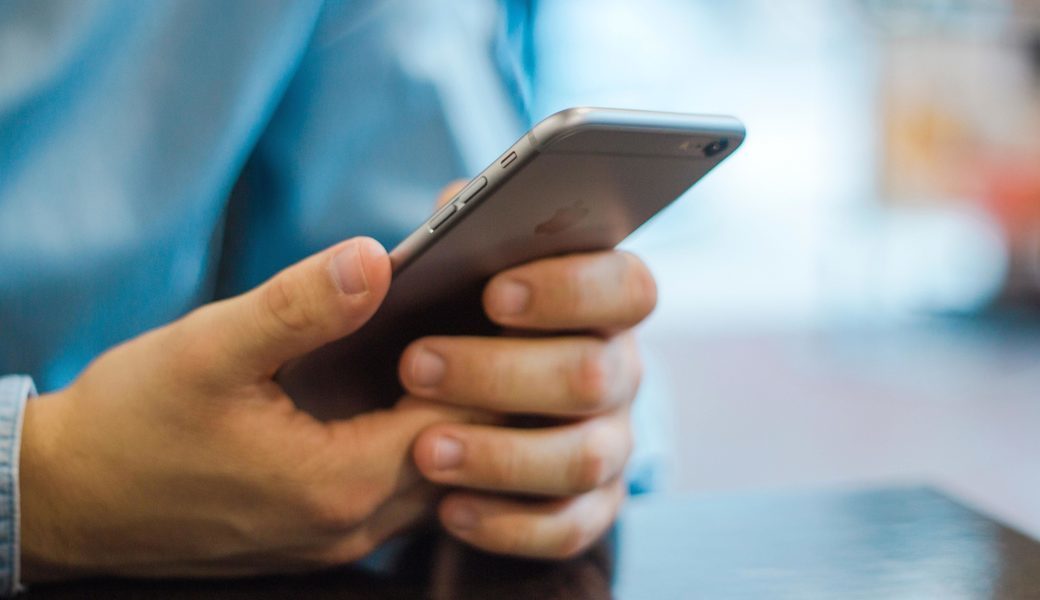 White hands hold a slim, black smartphone.
