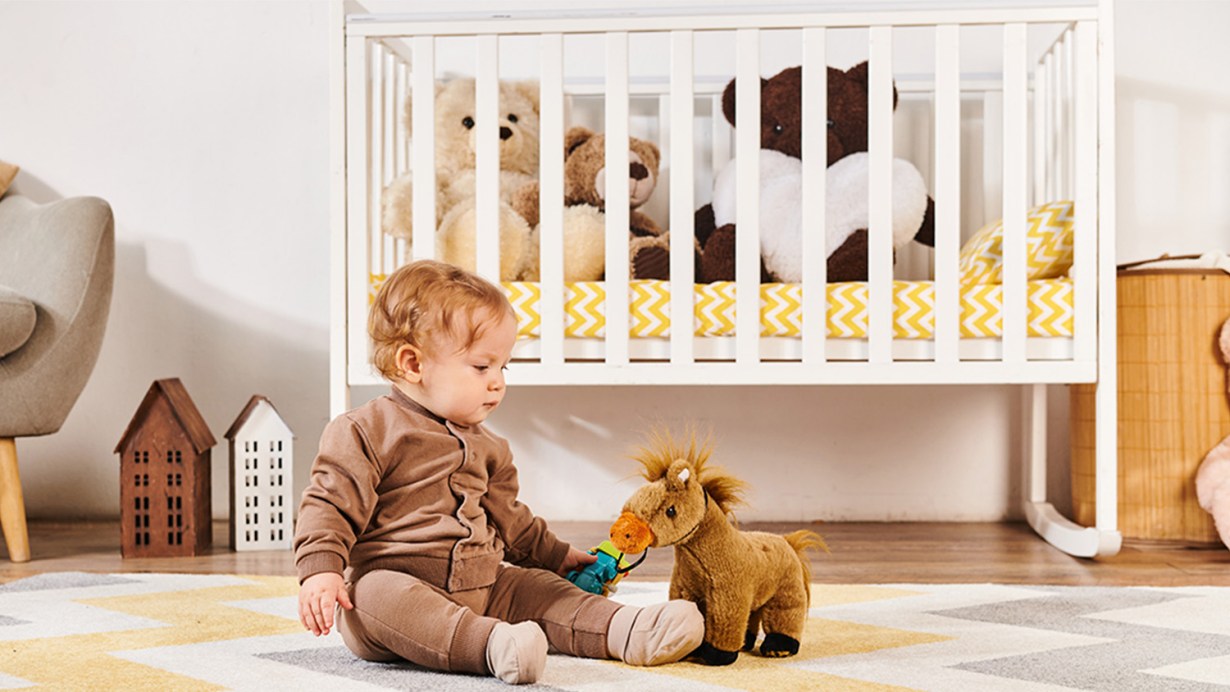 A baby sitting on the floor in front of a small crib